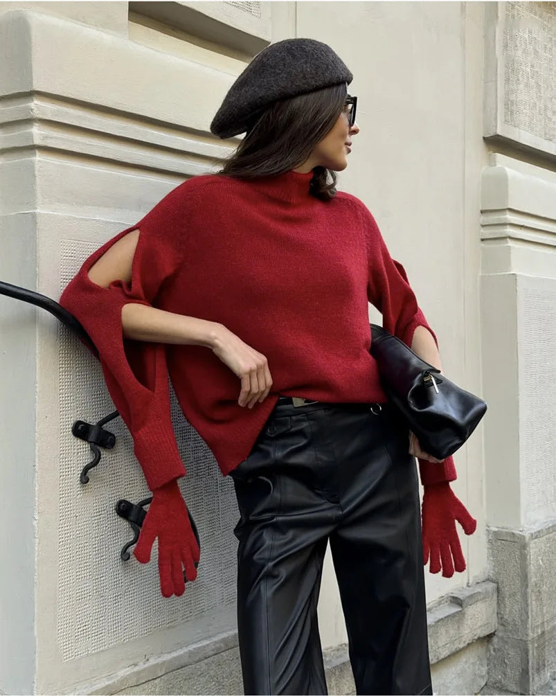 Person wearing a red sweater, black pants, and red gloves leaning against a stone wall.