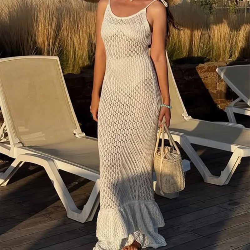 Woman in a white crochet dress standing by lounge chairs on a wooden deck.