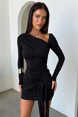 Woman wearing a black one-shoulder dress against a white wall.