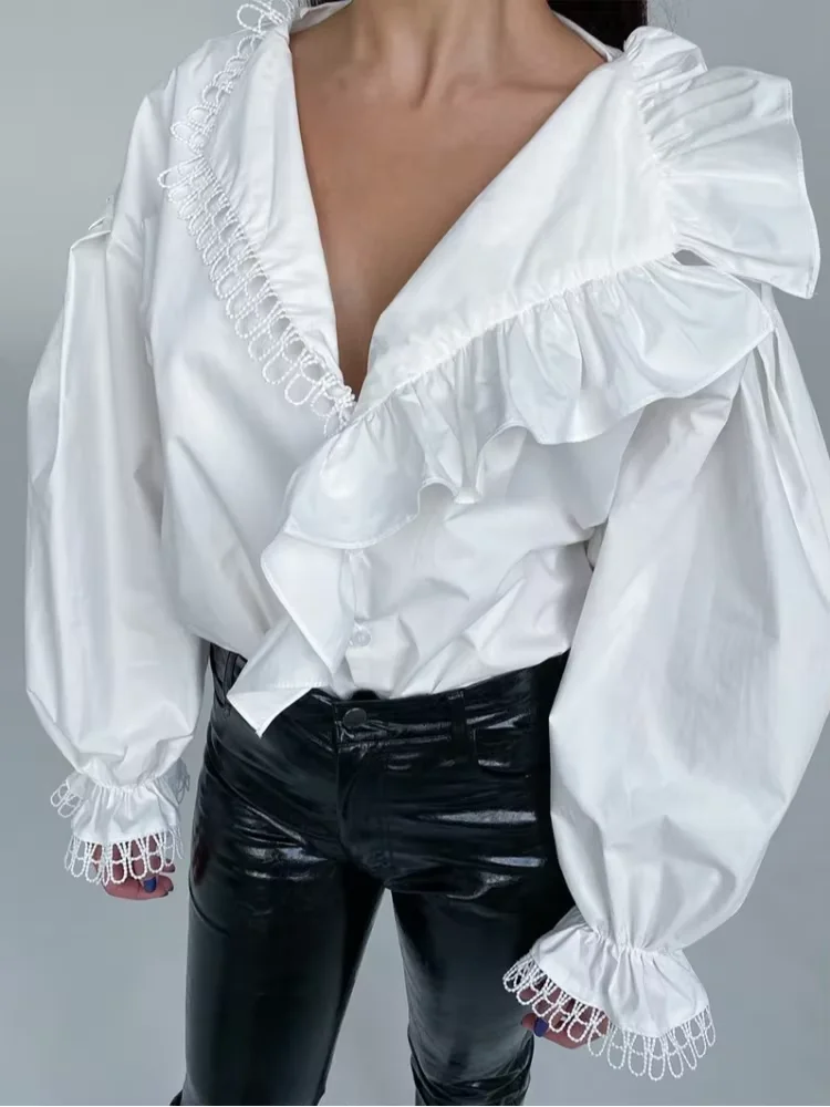 White blouse with ruffled details and black pants on a gray background