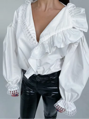 White blouse with ruffled details and black pants on a gray background