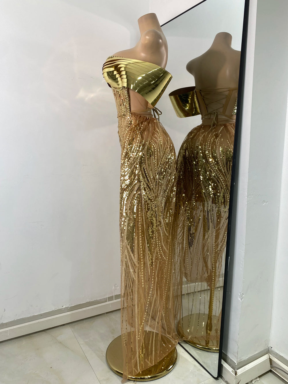 Gold sequin evening gown on a mannequin with a mirror reflection.
