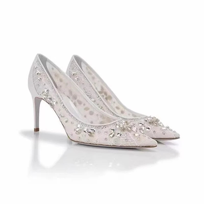 Pair of white high-heeled shoes with crystal embellishments on a white background