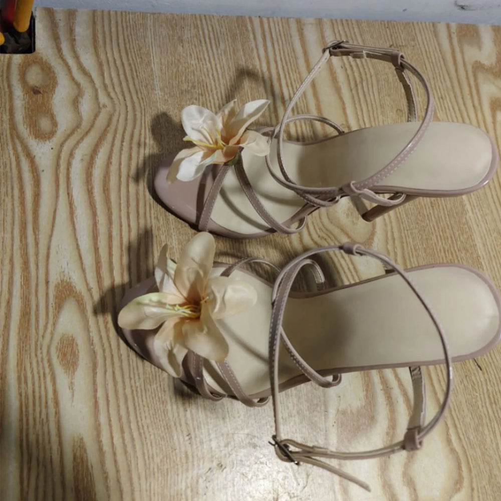 Pair of beige sandals with floral decorations on a wooden surface