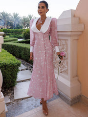 Woman in a pink dress with white accents standing in an outdoor setting.