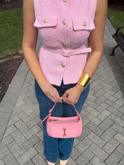 Person wearing a pink textured vest and holding a matching pink handbag on a paved walkway.