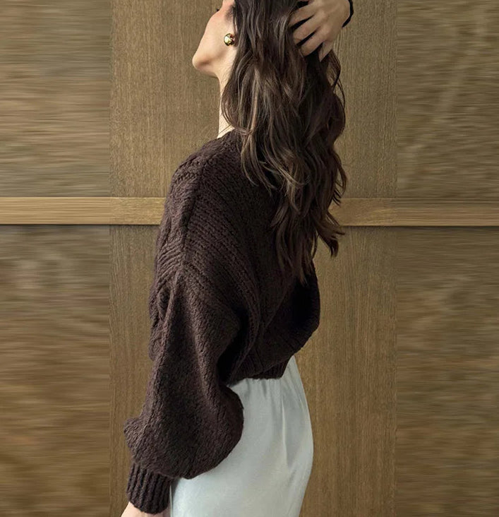 Woman wearing a dark brown sweater and light-colored pants against a wooden panel background