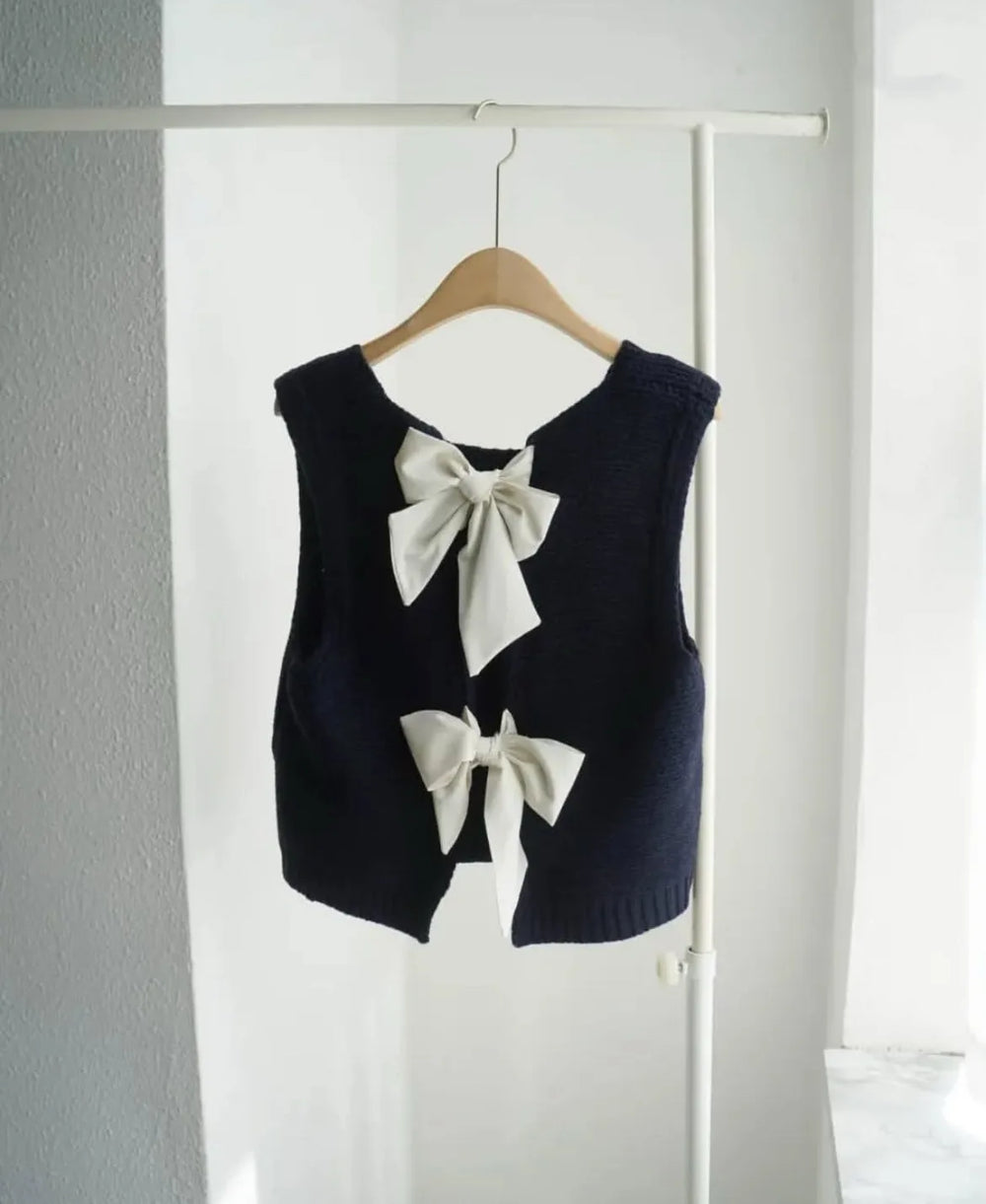 Navy blue sleeveless sweater vest with white bows on a hanger against a white wall.