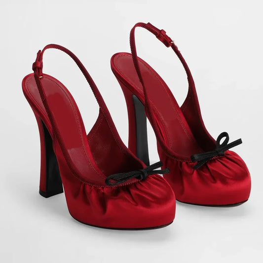 Red satin slingback platform pumps with a black bow detail.