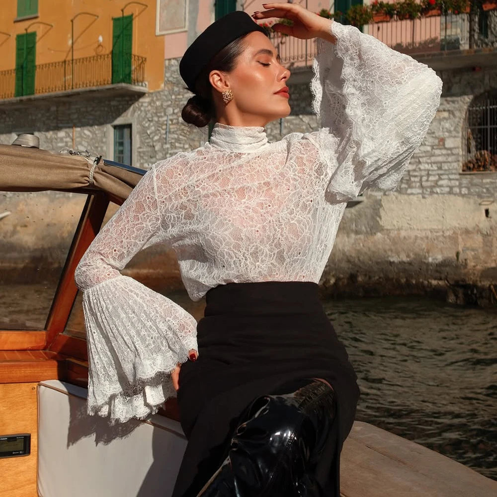 Woman in a lace top and black skirt sitting on a boat by a waterfront.