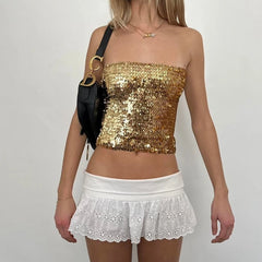 Person wearing a gold sequin top and white skirt with a black bag on a plain background