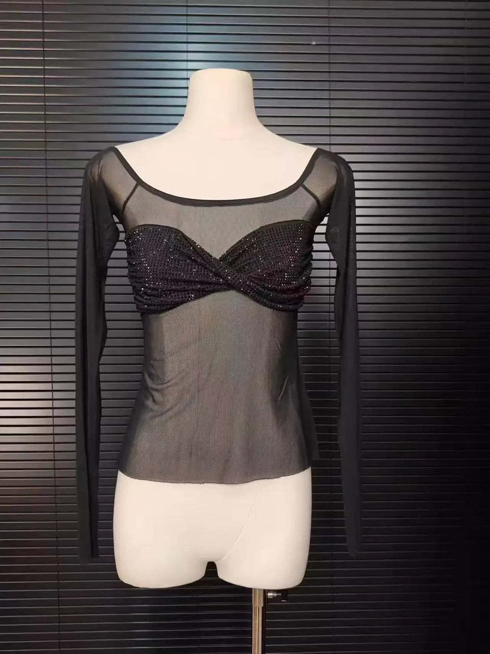 Black sheer top with glittery detailing on a mannequin against a dark background