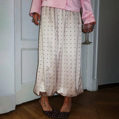 Person wearing a pink top and polka dot pants, holding a glass, standing in a room.