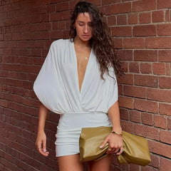 Woman in a white dress holding a gold clutch against a brick wall