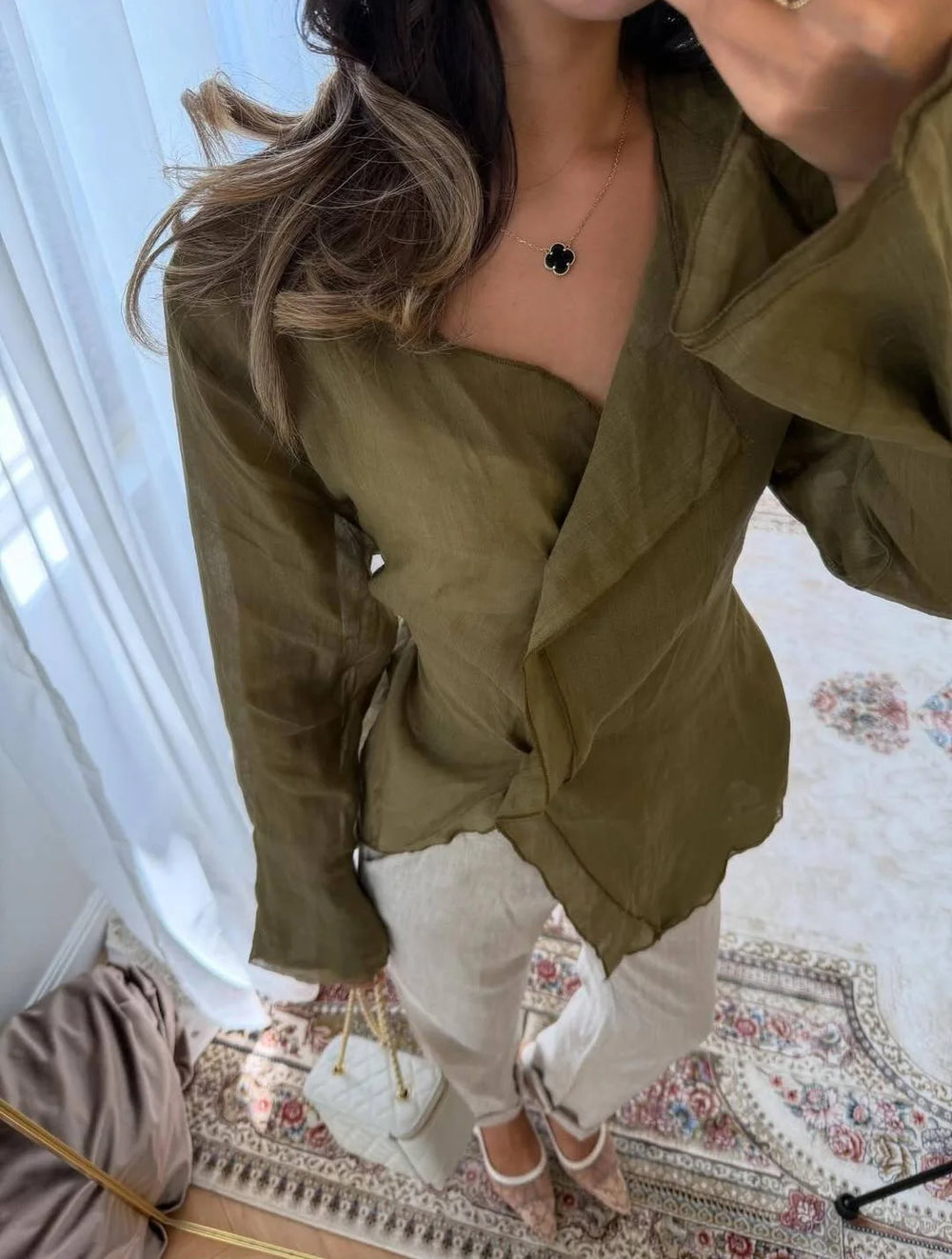 Person wearing a green jacket and white pants in a room with a floral rug.