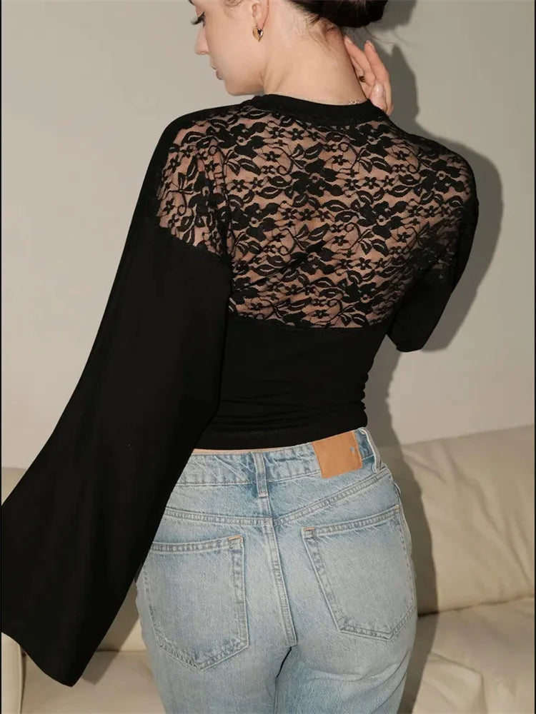 Person wearing a black lace top and blue jeans with a beige background