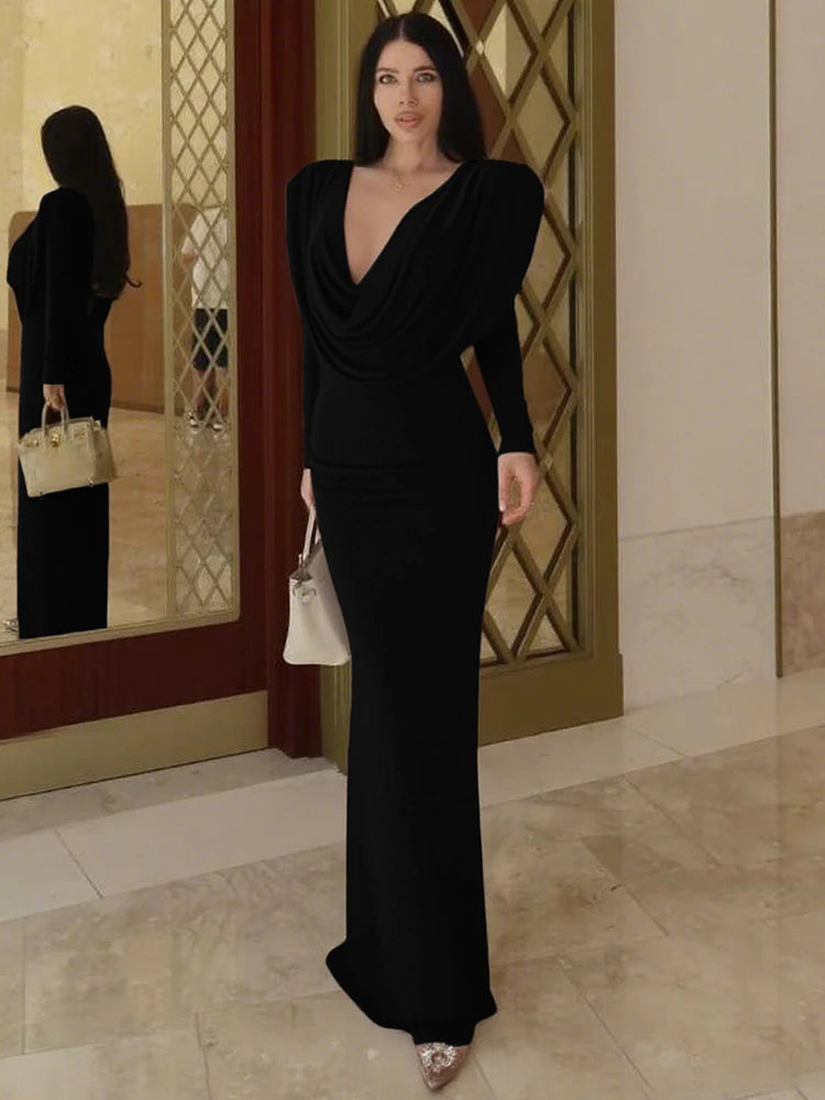 Woman in a black evening gown standing in a stylish interior setting.