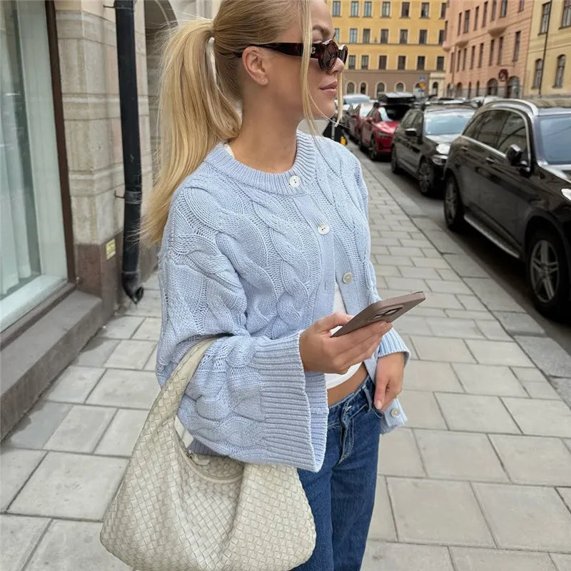 Woman in a light blue cable knit cardigan and jeans walking on a city street.