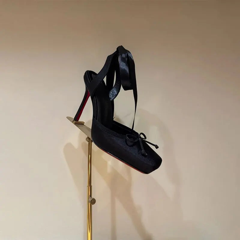 Black high-heeled shoes with red soles on a gold stand against a beige wall