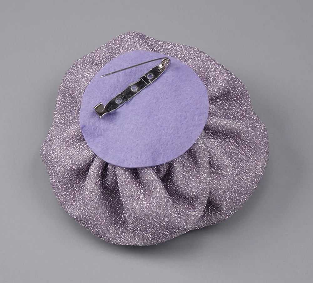 Silver glittery bag with a purple circle and hair clip on a gray background