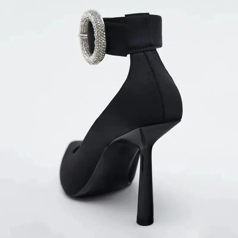Back view of black pointed toe pump with rhinestone ankle strap buckle and stiletto heel.