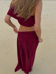 Back view of a woman in a burgundy ruched crop top and maxi skirt on a beach