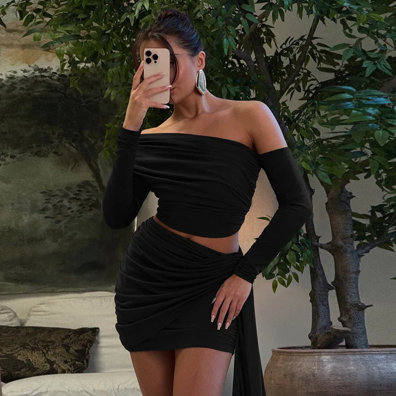 Woman in a black outfit taking a mirror selfie in a room with plants and a painting.