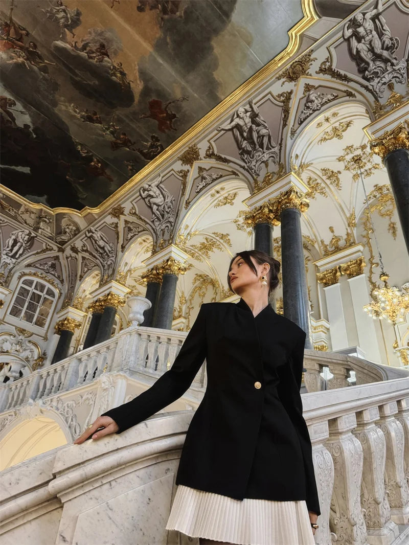 Woman in a black coat standing in an ornate interior setting