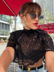 Woman wearing a black lace top with sunglasses and red lipstick, standing outdoors.