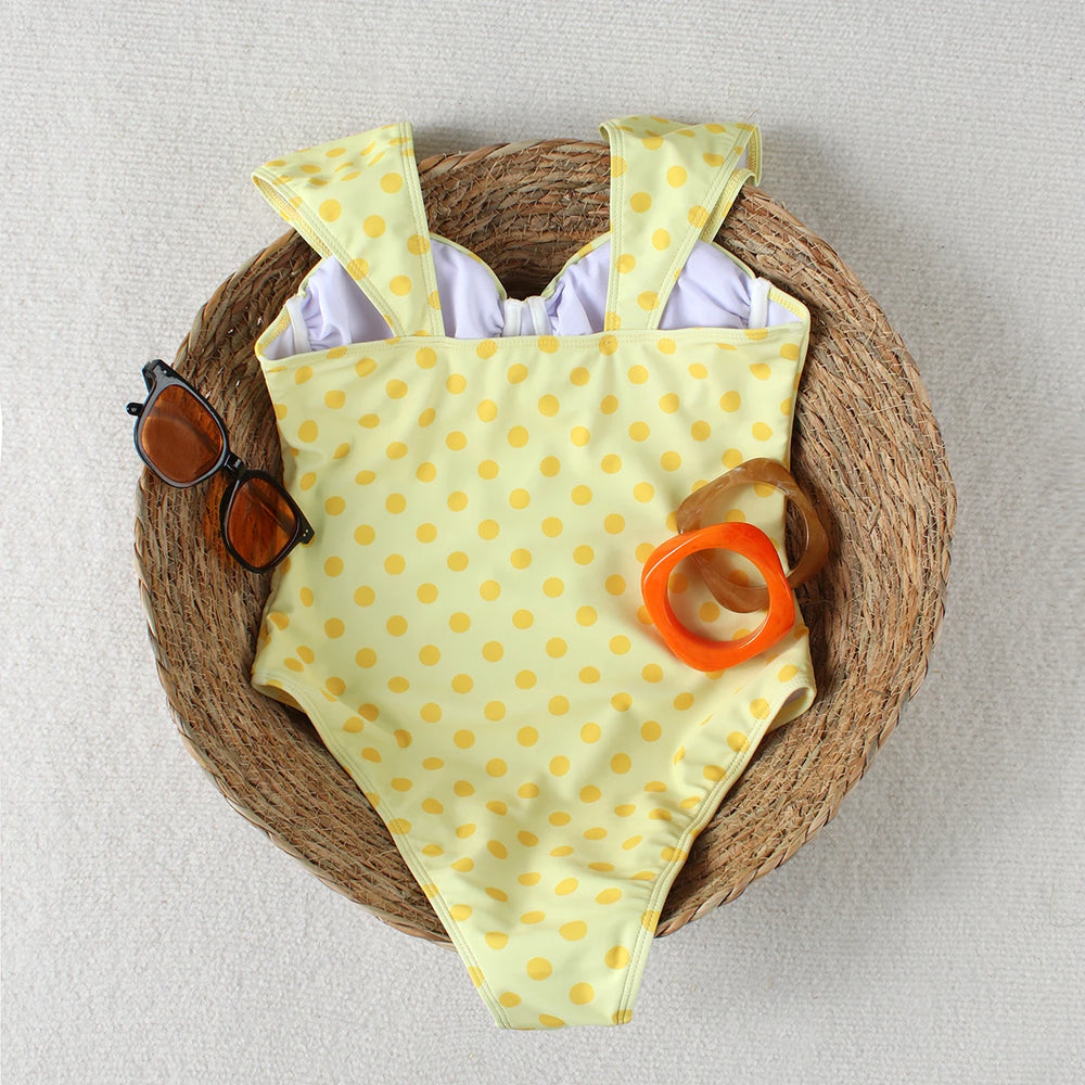 Back view of a yellow polka dot one piece swimsuit laid flat in a woven basket