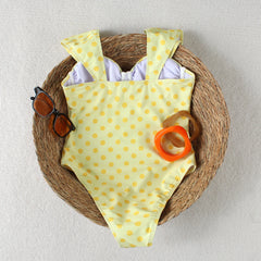 Back view of a yellow polka dot one piece swimsuit laid flat in a woven basket
