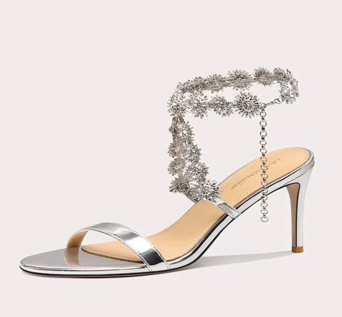Silver high-heeled sandal with decorative chain on a white background