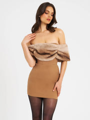 Woman wearing a tan dress with a fur shrug on a white background