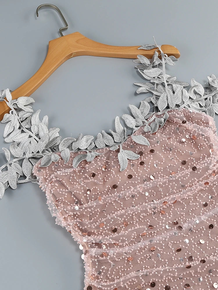 Pink sequined fabric with floral lace trim on a wooden hanger against a gray background