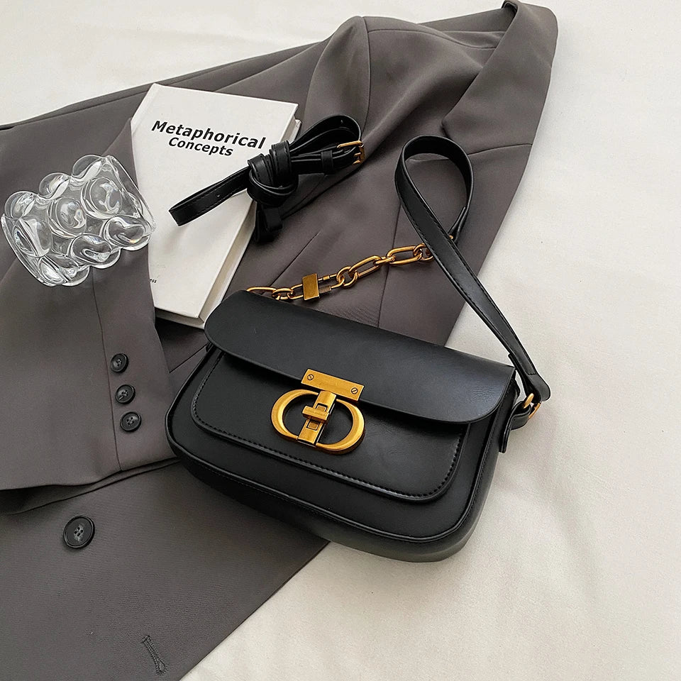Black handbag with gold clasp on a gray coat with books and a bracelet.