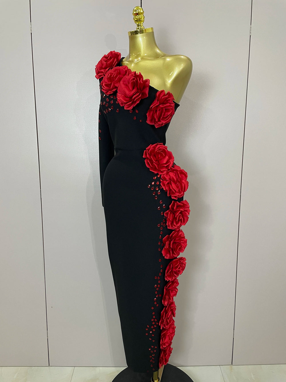 Black evening gown with red floral decorations on a mannequin against a white background