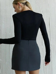 Person wearing a black long-sleeve top and gray skirt against a textured white wall.