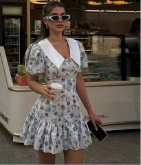 Woman in a floral dress holding a coffee cup in front of a store.