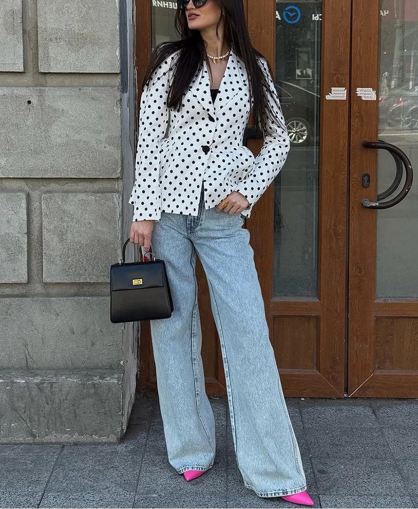 Woman in a polka dot blouse and jeans standing in front of a building entrance.