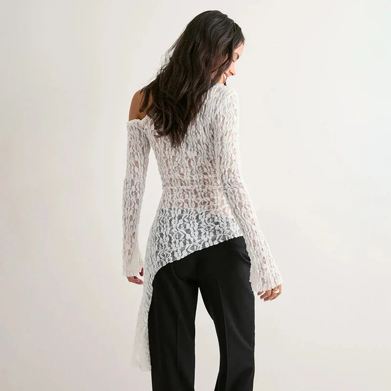 Woman wearing a white lace top and black pants against a plain background