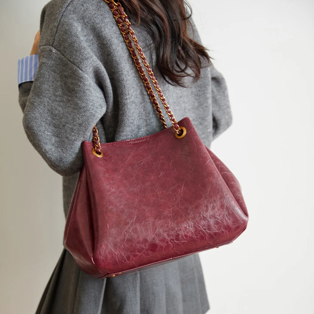 Person holding a red handbag with a chain strap against a neutral background