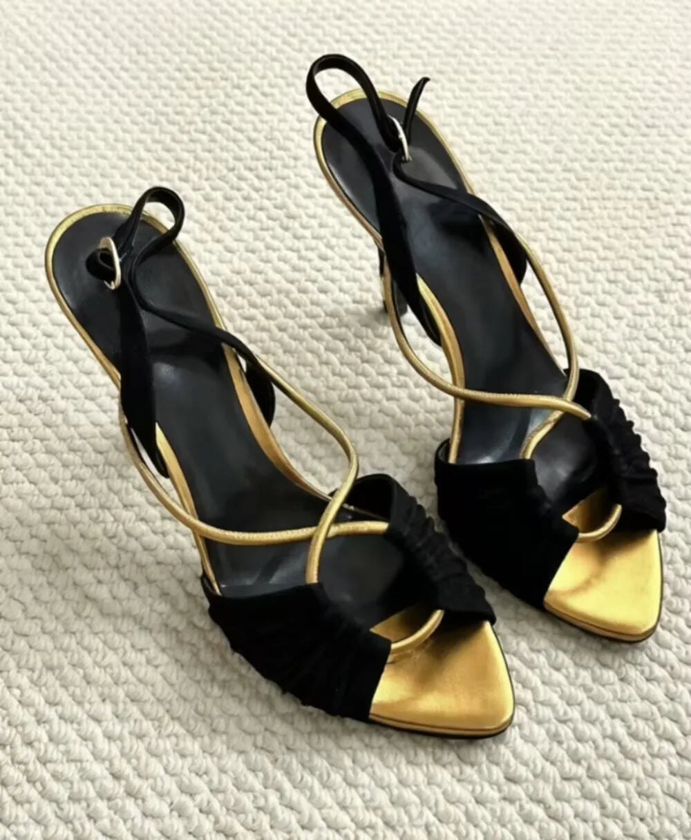 Pair of black and gold stiletto heeled sandals on a white textured surface