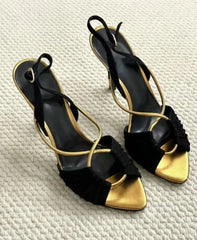 Pair of black and gold stiletto heeled sandals on a white textured surface