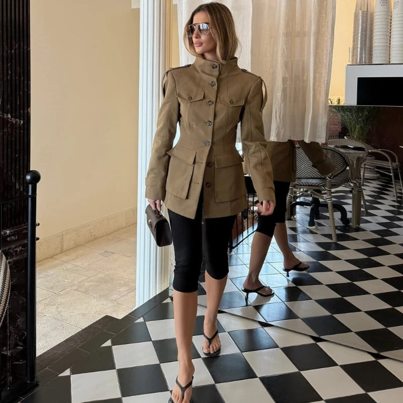 Woman in a beige jacket standing on a black and white checkered floor.