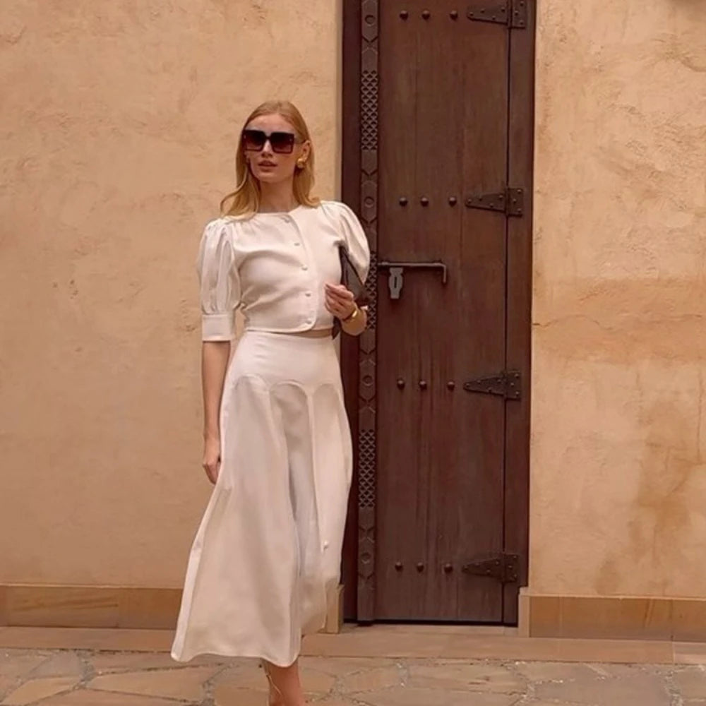 Woman in a white outfit standing in front of a textured wall with a wooden door.