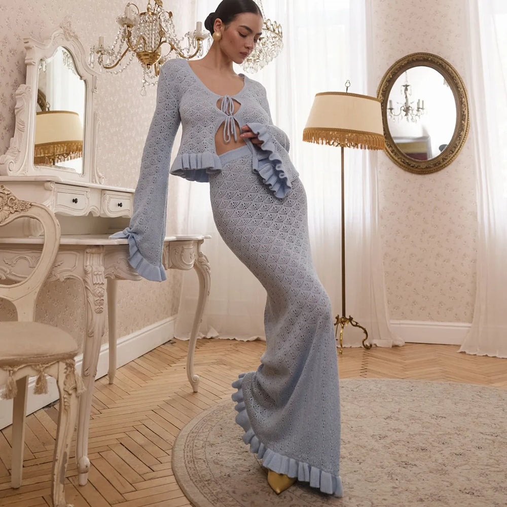 Woman in a light blue outfit standing in an elegant room with chandeliers and a mirror.