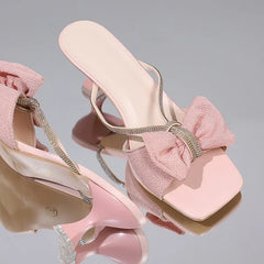 Pink high-heeled sandals with decorative bows on a reflective surface