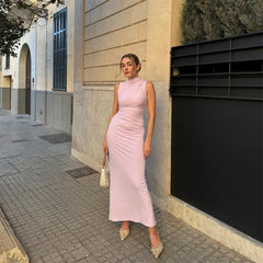 Woman in a pink dress standing on a sidewalk next to a building.