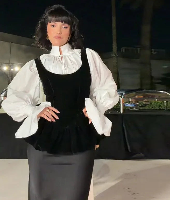 Person wearing a black pinafore over a white blouse with a dark background