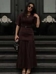 Woman in a dark brown dress standing on steps with a black door in the background